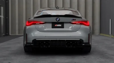 Rear View Of Grey Bmw M4 G82 Parked In Industrial Space Featuring Carbon Fibre Spoiler And Quad Exhaust