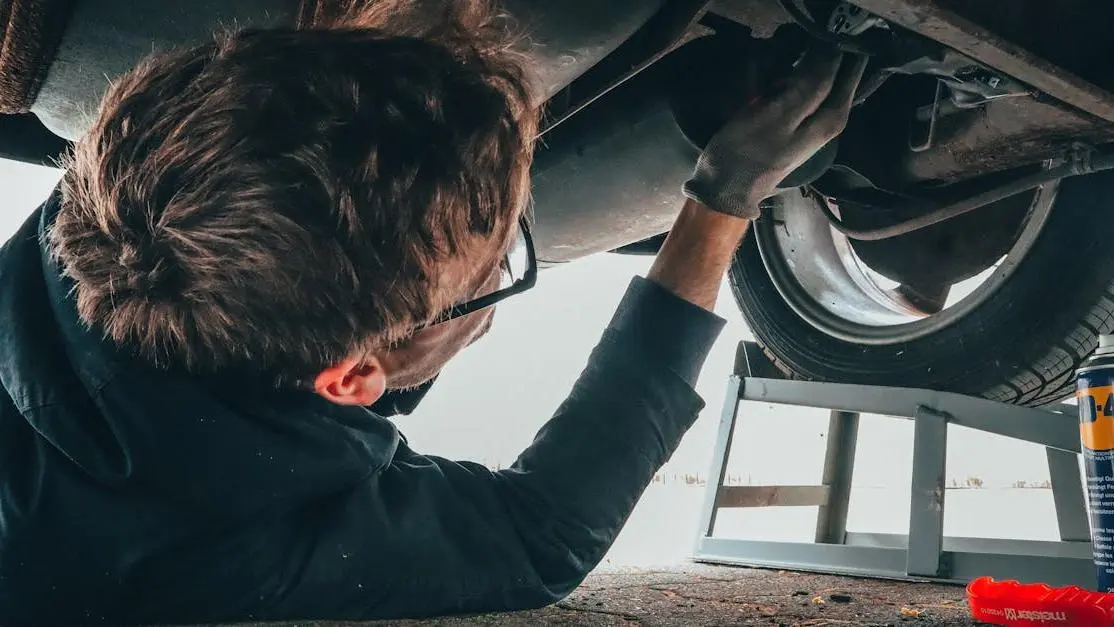 Mechanic installing rear diffuser on car undercarriage outdoors.