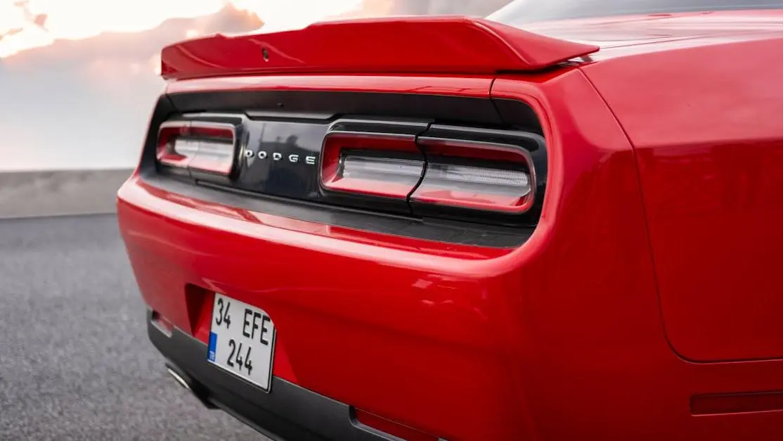 Red Dodge sports car rear at sunset road, showcasing sport exhaust systems and taillight